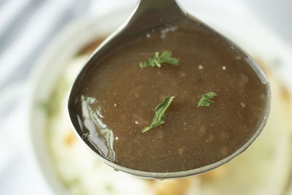 Horizontal image of homemade brown gravy in a ladle with parsley flakes.