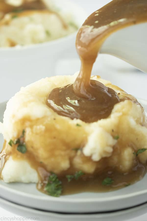 Beef Gravy pouring from boat on to mashed potatoes on a gray plate.