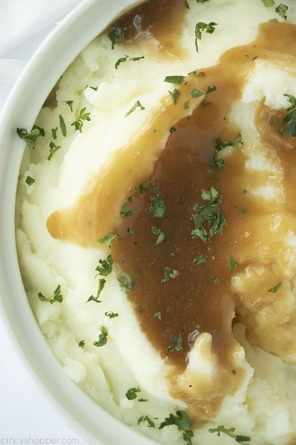Mashed potatoes in a white dish with brown gravy and green parsley flakes.