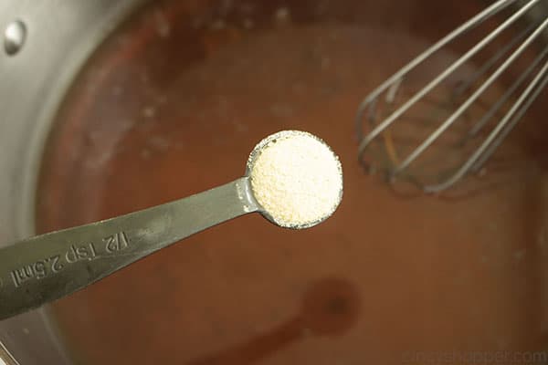 Spices in a measuring spoon being added to stainless pot with whisk in the background