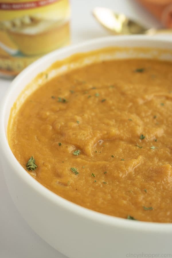 Easy Pumpkin Soup on a white bowl with white background. Can of pumpkin and a spoon in the background..