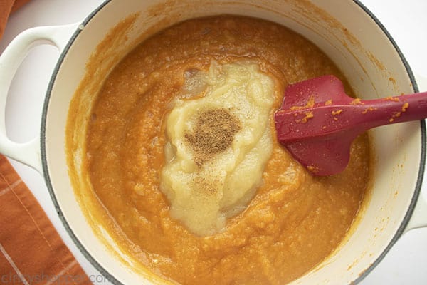 Applesauce and nutmeg on top of soup in white pan red spatula off to the side