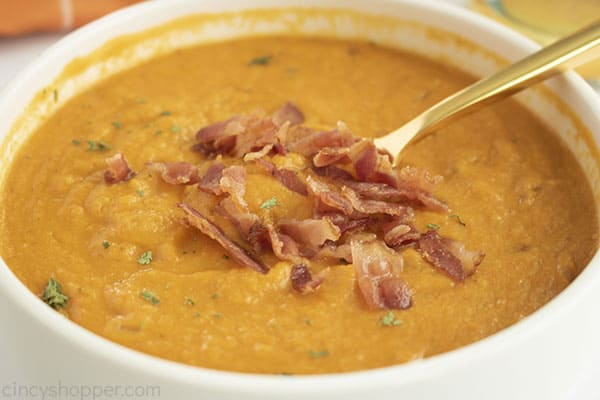 White bowl with soup with bacon topping spoon off to side