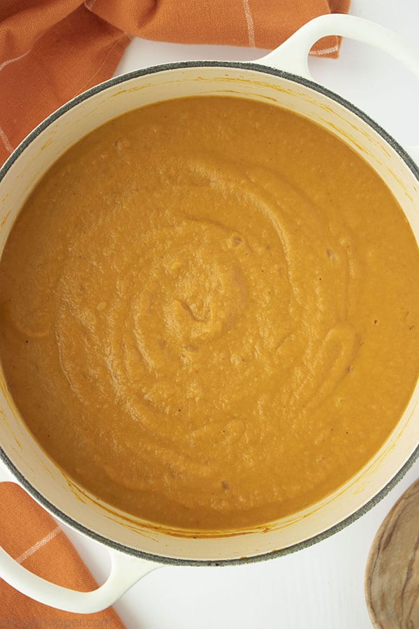 White background with pot of Easy Pumpkin soup. Orange towel off to the side.