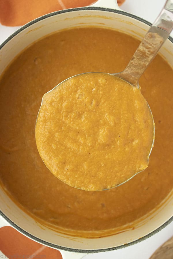 Ladle with pumpkin soup over the top of a white pot