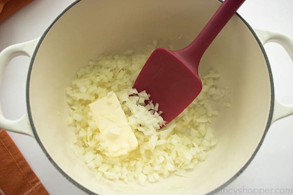 Butter and onions added to a white pot with red spatula in the pan