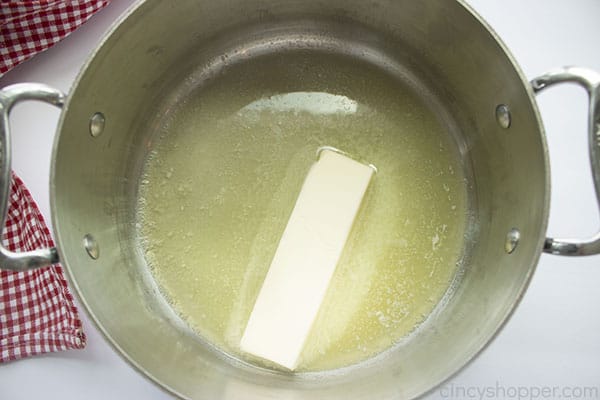 Melting butter in a stainless pot with white background includes red and white checkered towel.