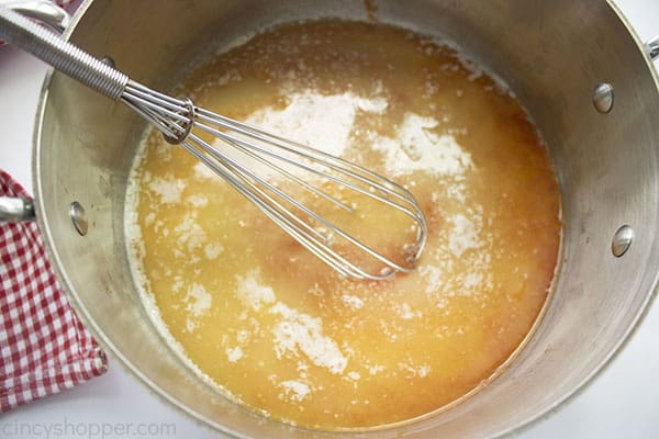 Franks red Hot Sauce added to melted butter pan with a whisk white background and reed white checkered towel.