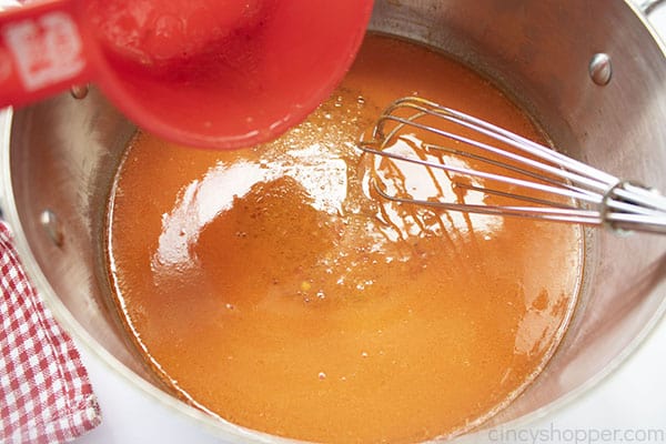 Red measuring cup of Wishbone Italian Dressing added to Red Hot mixture. whisk in pan.