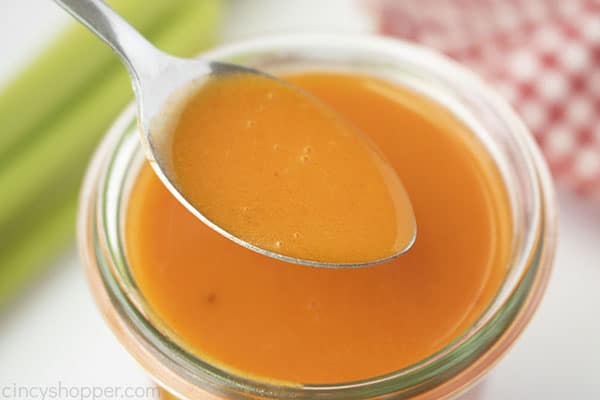 Horizontal image of Buffalo Sauce on a spoon. Celery and towel in background.