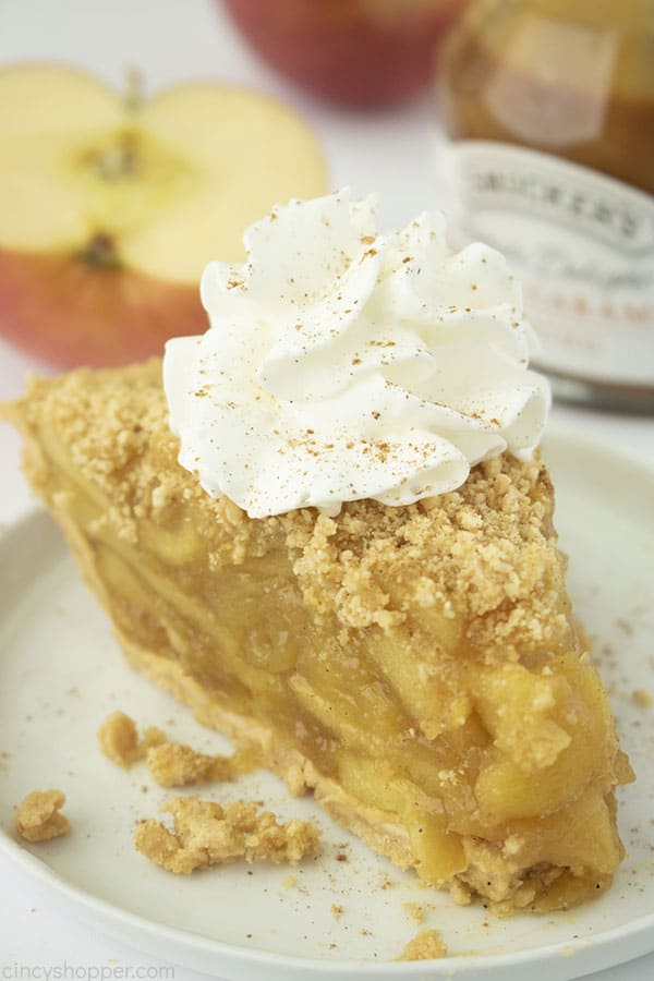 Slice of no bake apple pie with whipped cream on a white plate. Apple slices and caramel topping in backgroud.