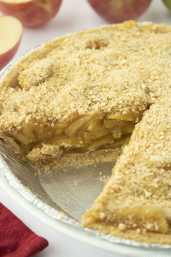 Whole apple pie with slice taken out. Apples in the background.