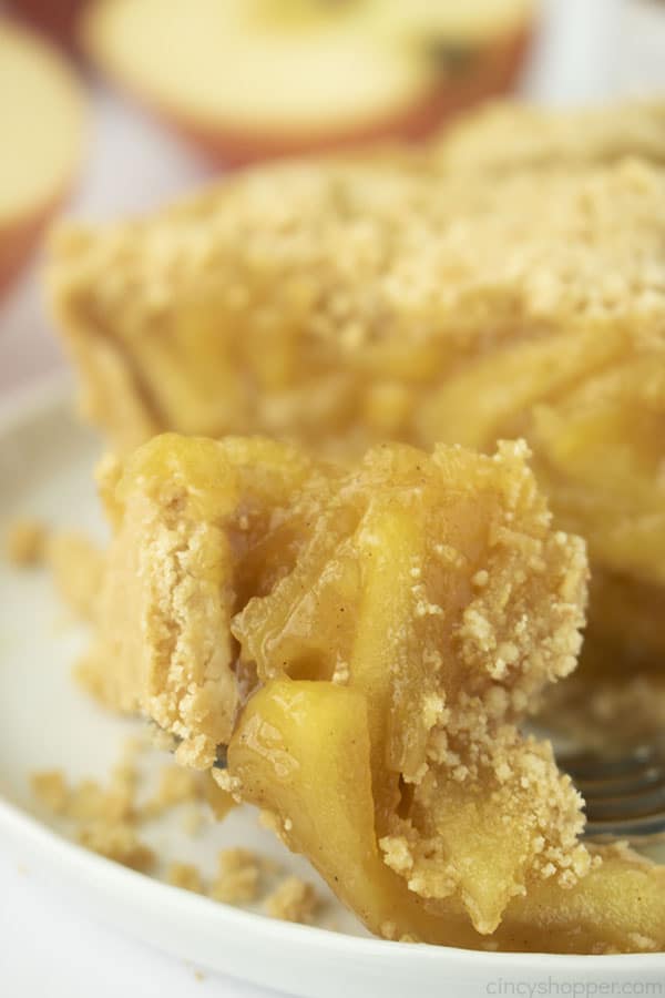 Apple pie on a fork with white plate. Apples in the background.