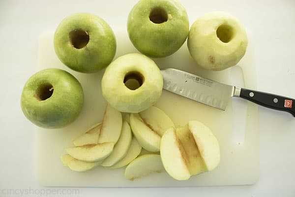 Cored and peeled green apples on a white cutting board with knife.