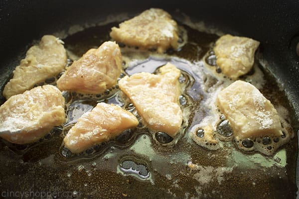 chicken frying in a dark pan