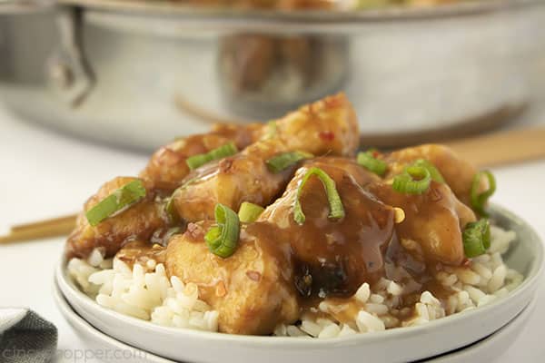 Homemade Chinese chicken over rice on a white plate and pan in background