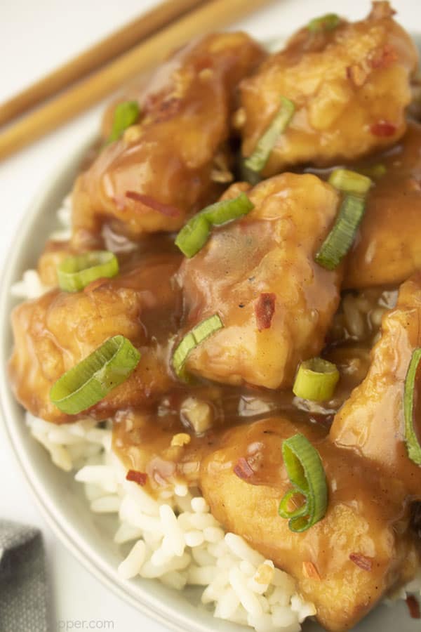 White plate with orange chicken on a white background with chopsticks