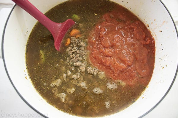 Ground beef, sauce, water, broth added to pot with red spatula