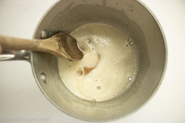 browned butter for frosting in saucepan with a wooden spoon on a white background