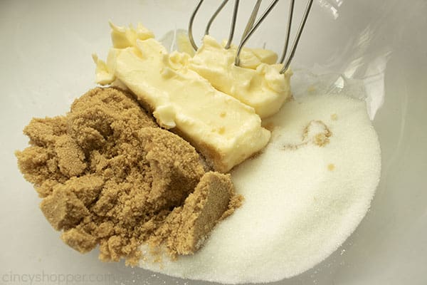 Butter and sugars in a clear bowl with beaters of to the side