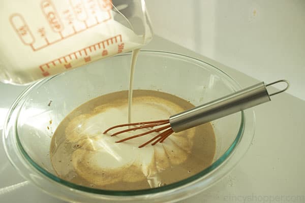 Clear bowl with cream being poured in. Whisk sitting in the bowl