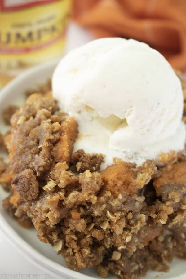 Pumpkin Crisp on a white plate with a scoop of vanilla ice cream on top. Pumpkin can and orange napkin in the background.