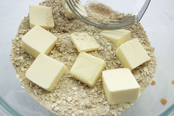 Butter added to crisp ingredients in a clear bowl with a pastry blender