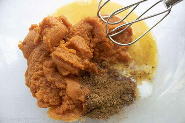 Pumpkin eggs and spices in a clear bowl with mixer beaters