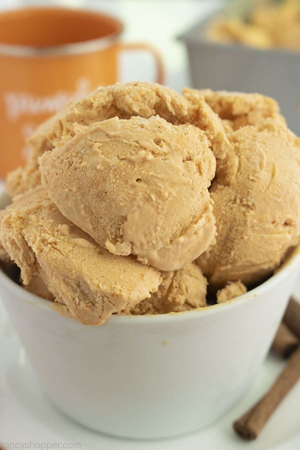 Scoops of Pumpkin Spice Ice Cream in a white bowl with mug and loaf pan in background