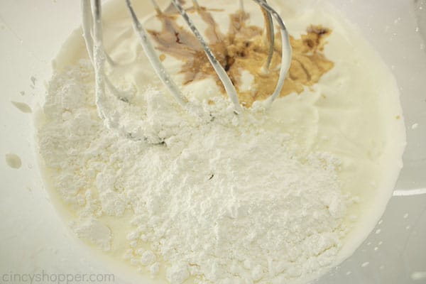 Close up image of whipped heavy whipping cream and dry ingredients added with a silver whisk 