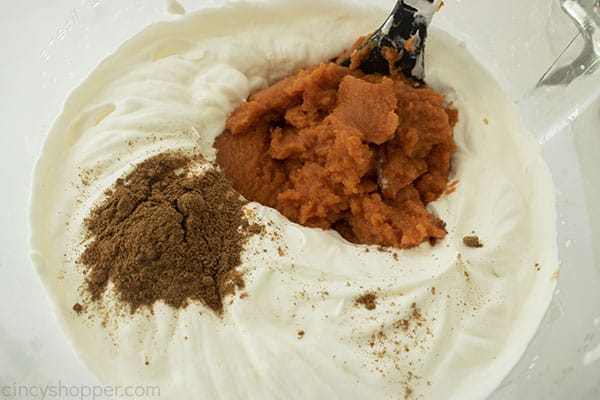 Close up image of whipped heavy whipping cream with a silver whisk and pumpkin spice and pumpkin puree