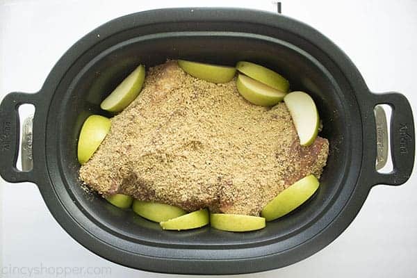 Overhead image of the Pulled Pork in a black oval Slow Cooker topped with the apple crisp rub and sliced green apples 