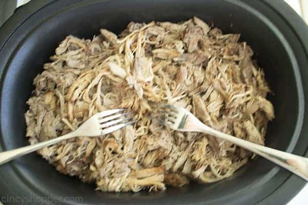 Overhead image of the Apple Cider Pulled Pork being pulled a part with two silver forks 