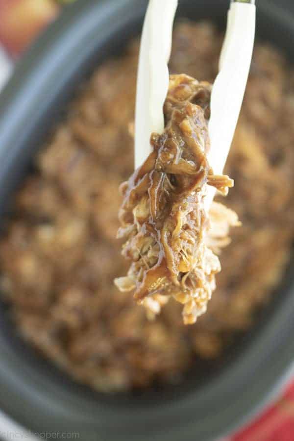 Close up photo of Slow Cooker Apple Cider Pulled Pork in silver tongs 
