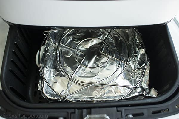 Baking dish covered in foil with metal rack for weight inside air fryer.