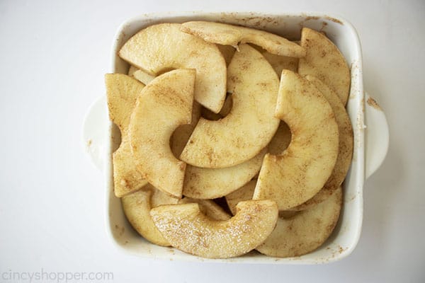 Sliced and coated apples in a small white baking dish