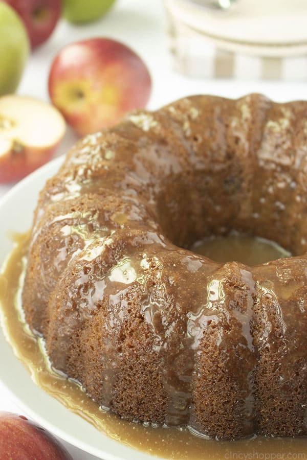 Glazed Apple Cake on a white plate with apples in the background.