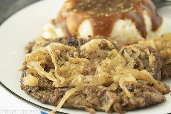 White plate with beef liver with mashed potatoes and gravy in background.