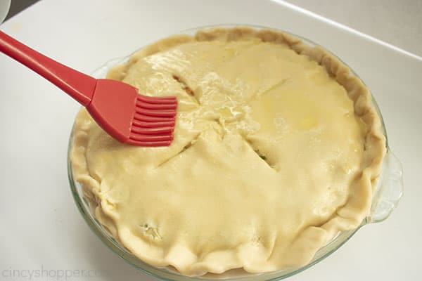 Pastry bush adding egg wash to top pie crust.