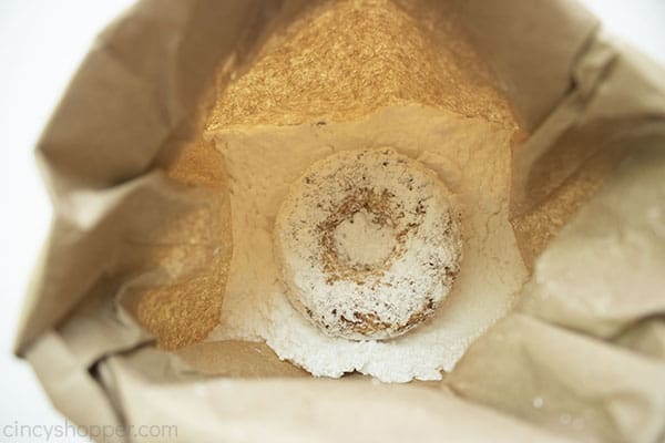 Baked donut in brown bag with powdered sugar.