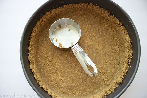 Crust in springform pan with measuring cup to shape