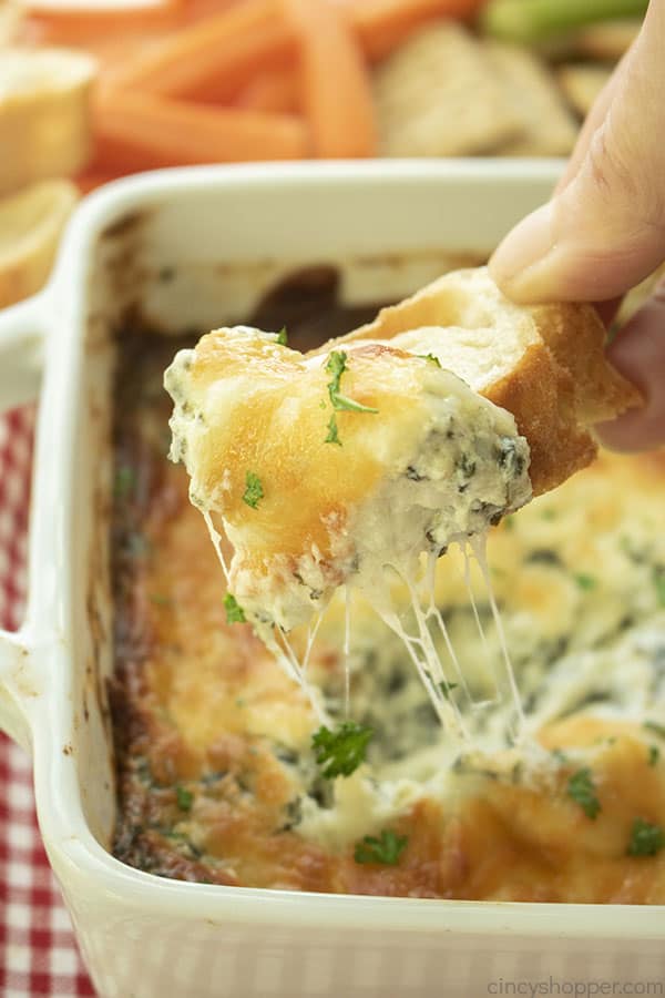 Hand dipping Cheesy Spinach Dip on bread