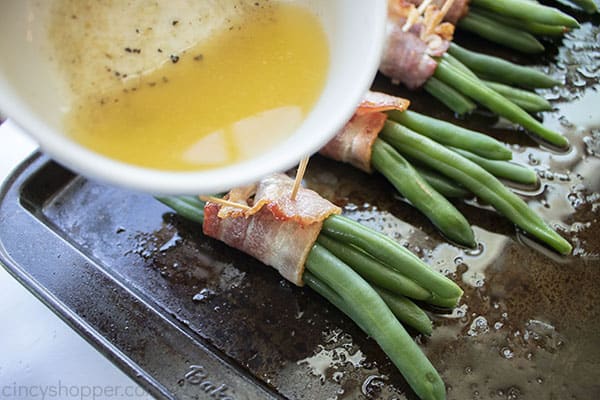 Drizzling butter and bacon grease mixture on to green bean bundles