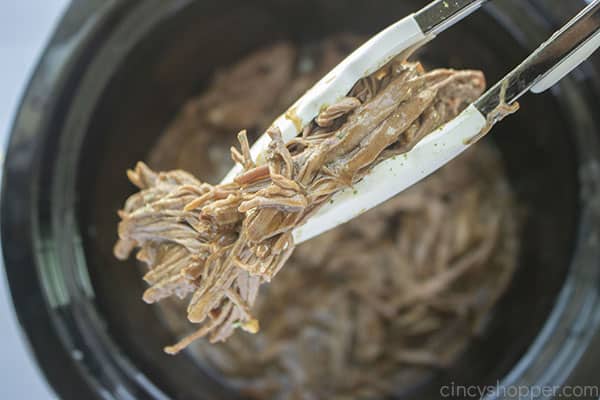 Shredded beef pot roast meat between tongs 