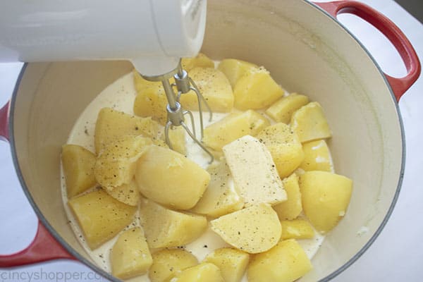 Cooked potatoes in pot with half and half, butter, salt, and pepper with mixer