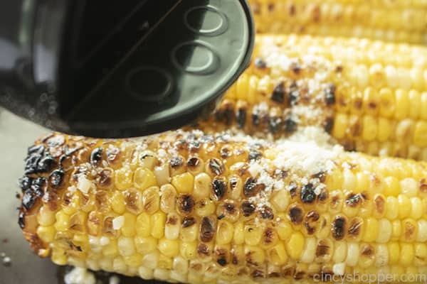 Adding parmesan cheese to grilled corn