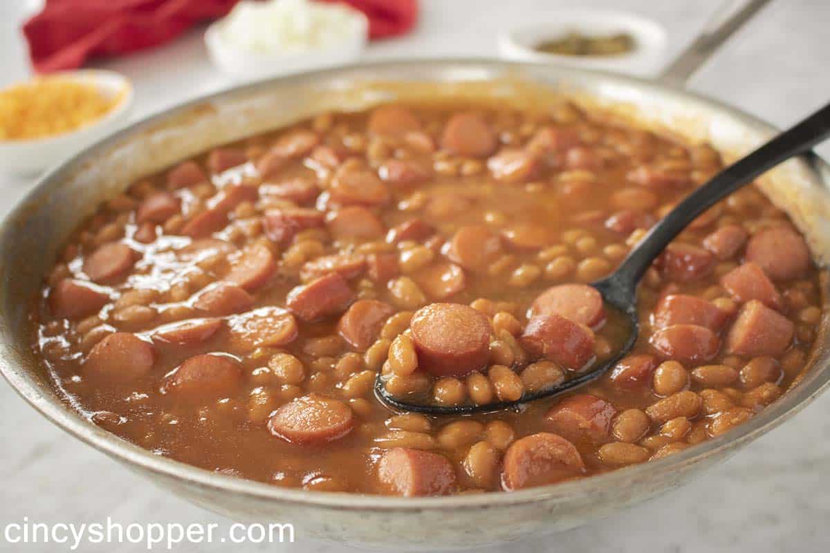 Hot dogs and beans in a pan with a spoon.