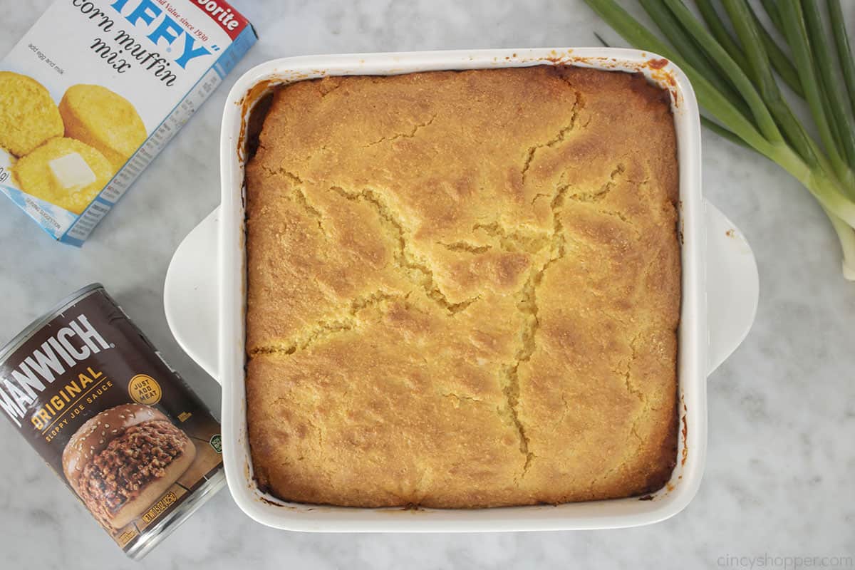 Sloppy Joe Casserole with cornbread in a white dish with Manwich, Jiffy mix and green onions on the side.