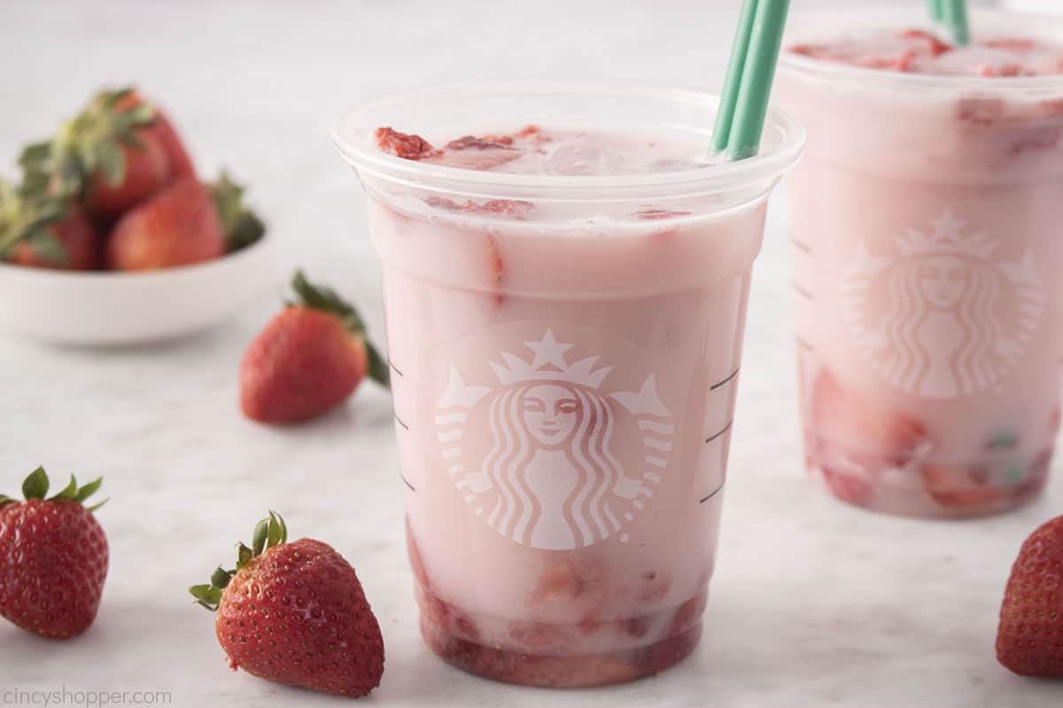 Pink Drink in a Starbucks cup with scattered strawberries.