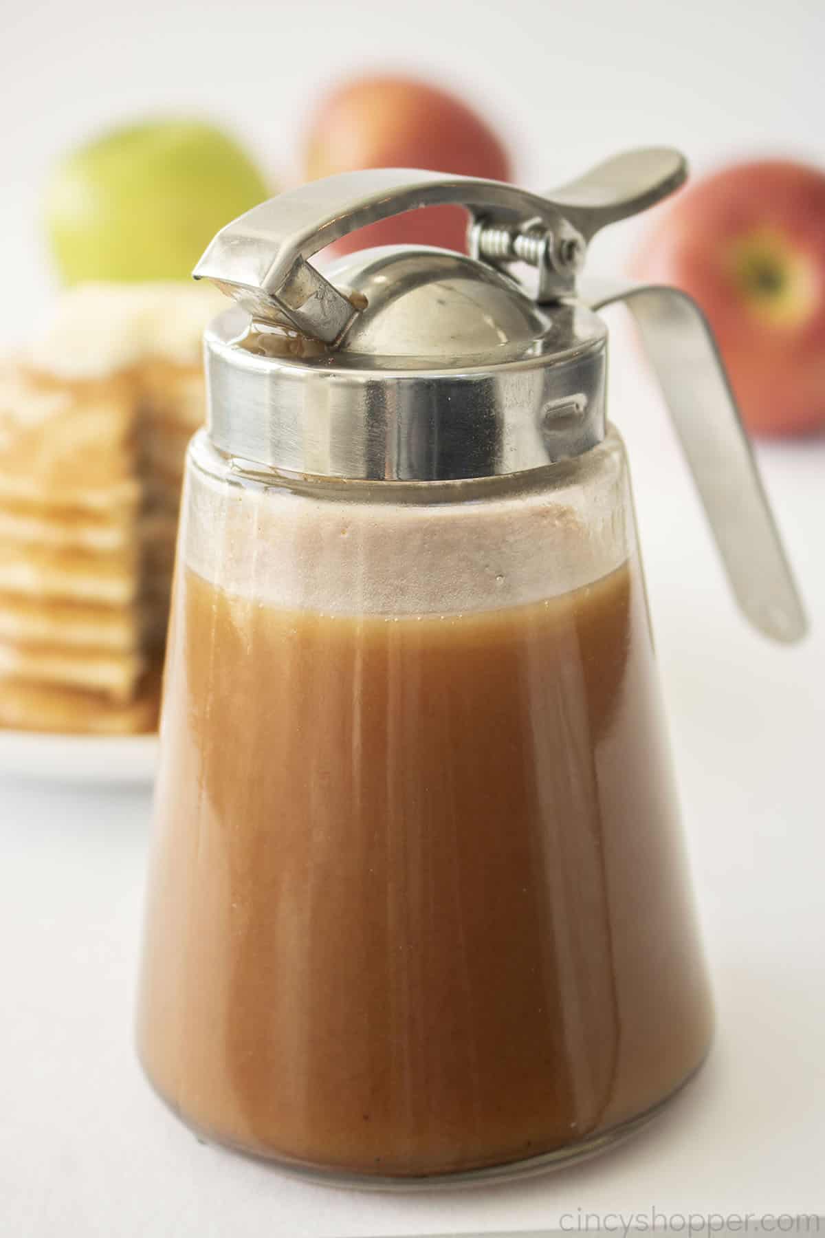 Apple Syrup in dispenser- apples in background.